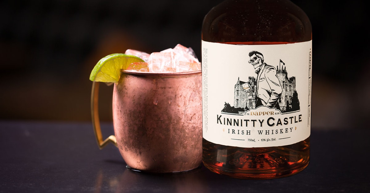 irish mule recipe image with a copper mug filled with an irish mule cocktail next to a bottle of kinnitty castle irish whiskey the dapper blend