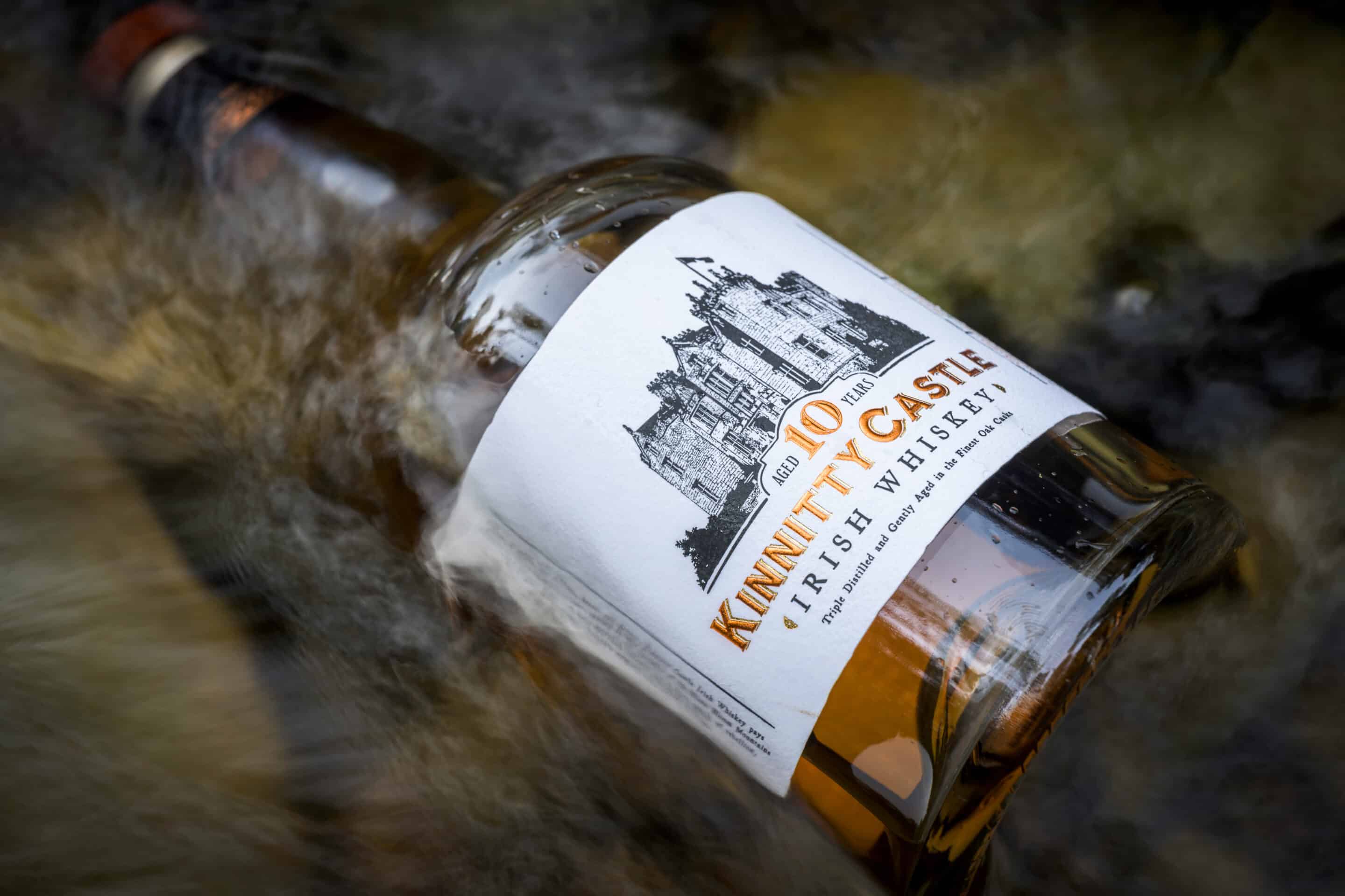 A bottle of Kinnitty Castle Irish Whiskey Aged 10 Years next to a bottle of Kinnitty Castle IRish Whiskey Dapper Blend on a table with a blurred background