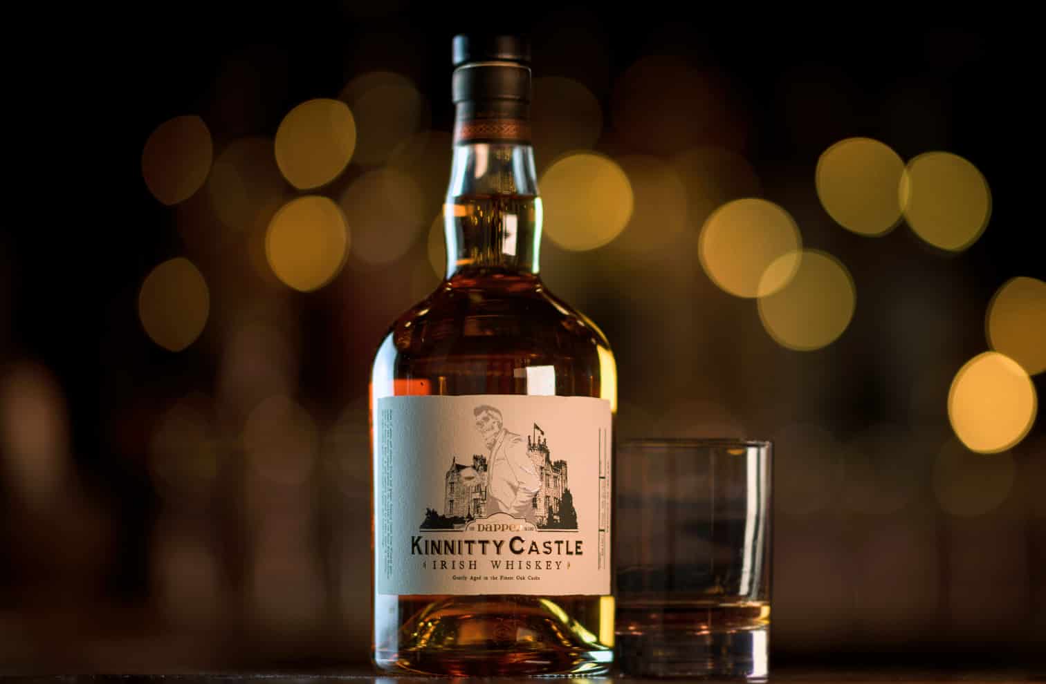 A bottle of Kinnitty Castle Irish Whiskey Aged 10 Years next to a bottle of Kinnitty Castle IRish Whiskey Dapper Blend on a table with a blurred background