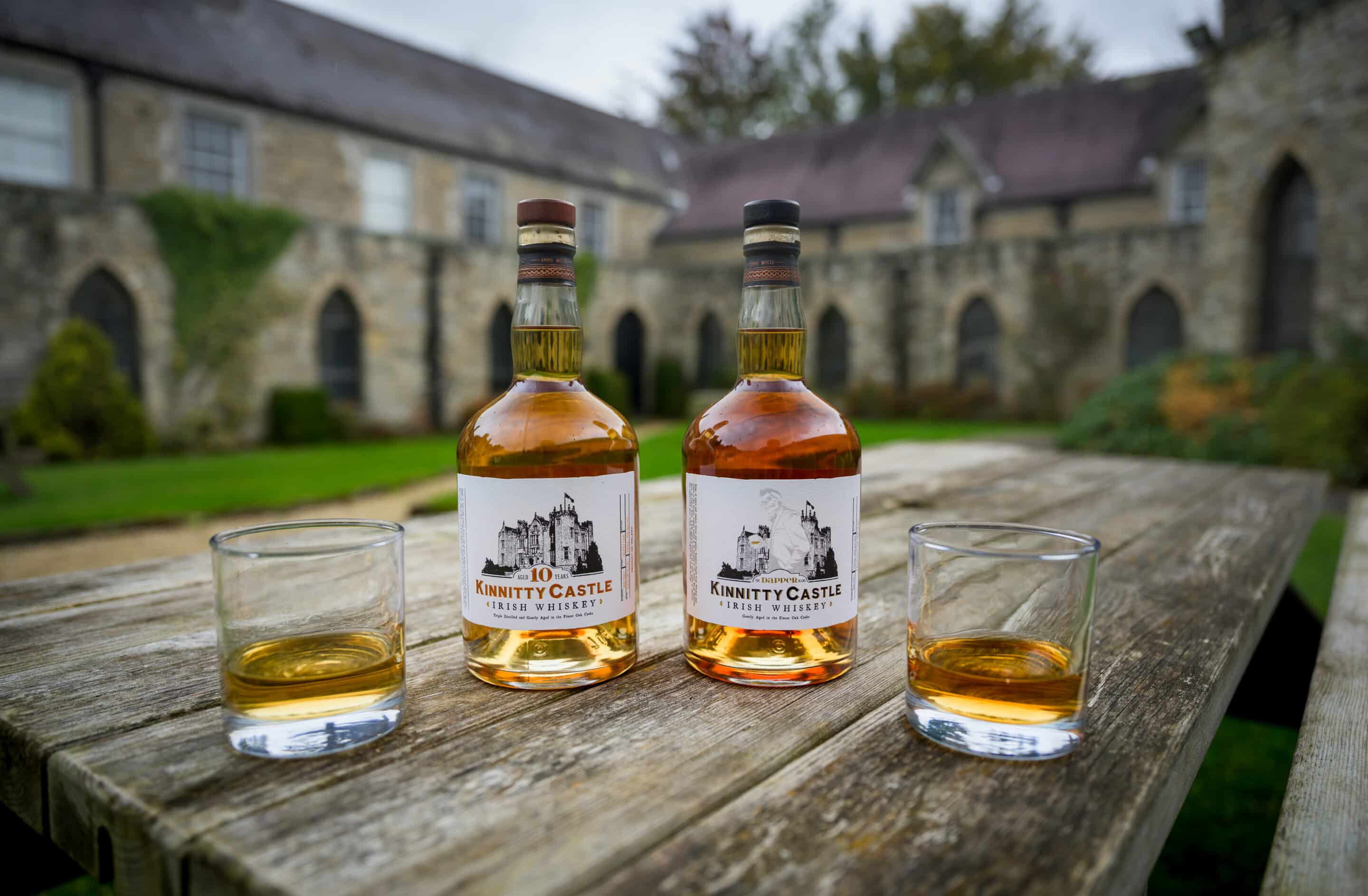 A bottle of Kinnitty Castle Irish Whiskey Aged 10 Years next to a bottle of Kinnitty Castle IRish Whiskey Dapper Blend on a table with a blurred background